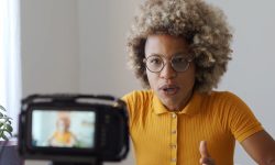 An African lady in a yellow blouse recording herself on a camera