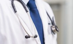 Detail of a stethoscope on the neck of a doctor with tie. Close up of a doctor with white lab coat stethoscope at hospital. Medical male doctor with lab coat and stethoscope at clinic.